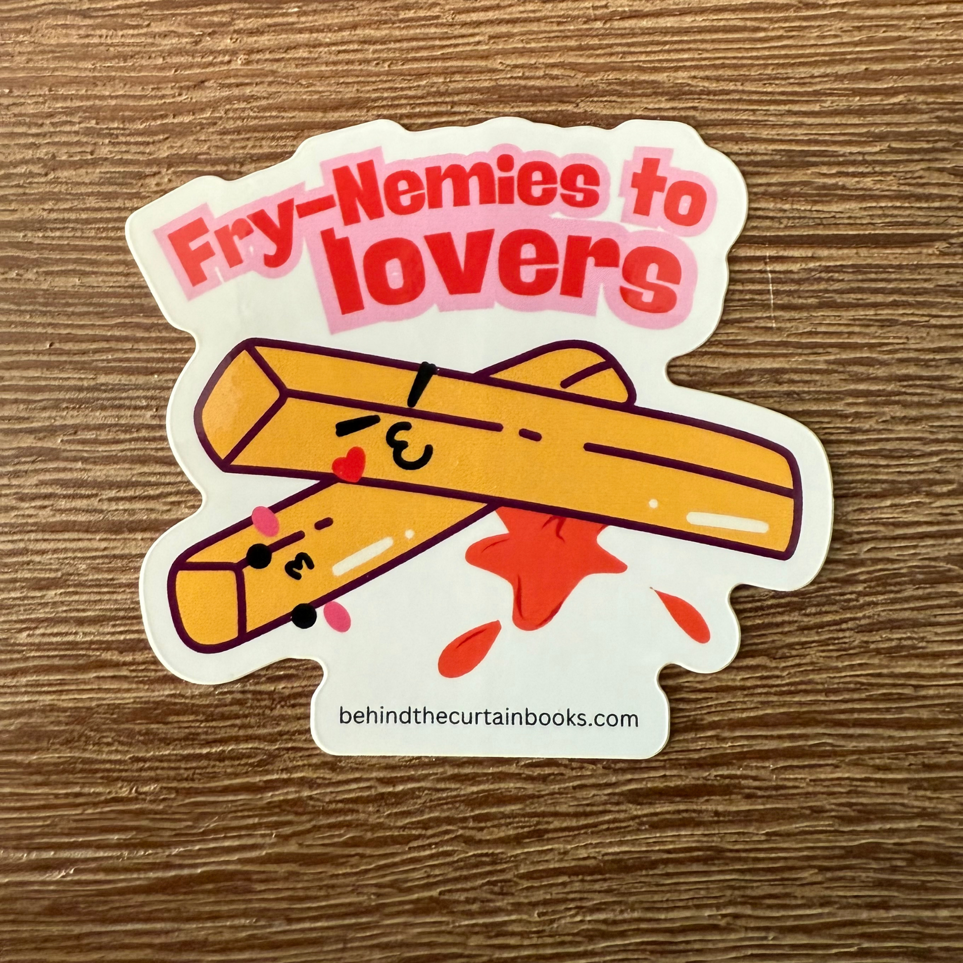 Sticker with two cartoon french fries and text 'Fry-Nemies to Lovers' on a wooden surface.