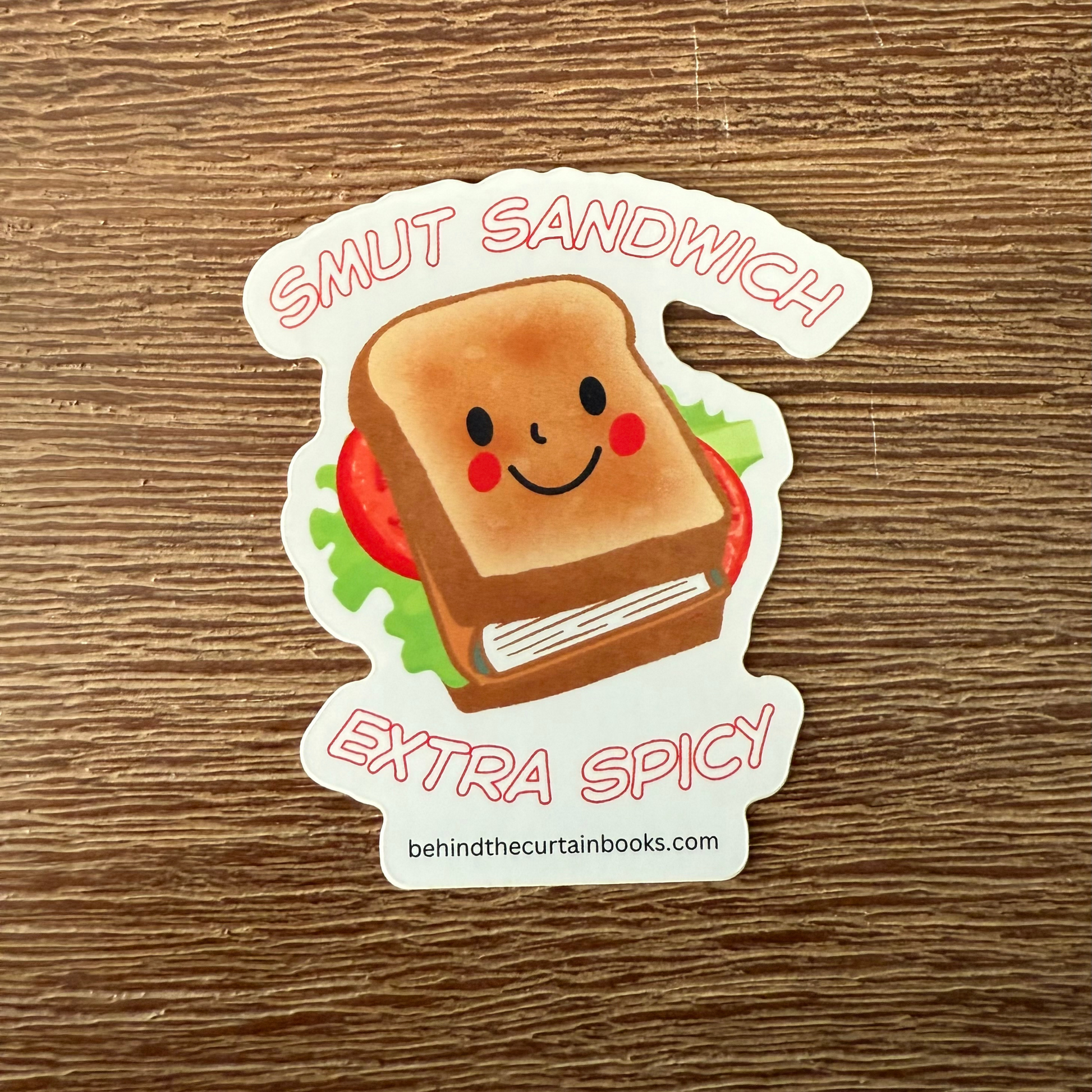 Sticker of a smiling sandwich with text 'Smut Sandwich Extra Spicy' on a wooden surface